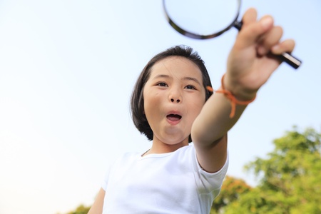 Asian little girl holding a magnifying glass in outdoorの写真素材