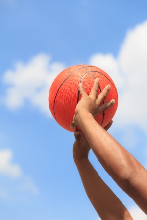 Basketball in hands on blue skyの写真素材