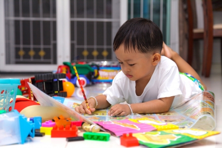 Happy little boy drawing and reading lying on the floor at homeの写真素材
