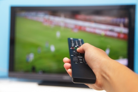 Hand pointing tv remote control towards the television as background 