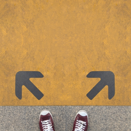 Pair of shoes standing on a road with two grey arrow on the yellow 