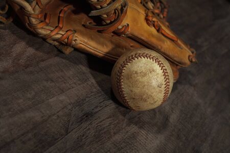 Old baseball glove with weathered baseball on wood backgroundの写真素材