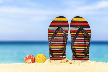 Flip flops on the sandy beach with blue sea and skyの写真素材