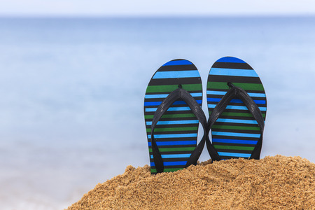 Flip flops on the sandy beach with blue sea and skyの写真素材