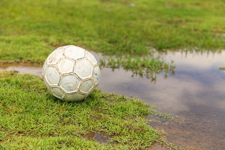 Old white soccer ball on the rough grass fieldの写真素材