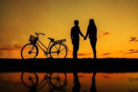 Silhouette of sweet couple in love happy time and bicycle in beautiful sunsetの写真素材