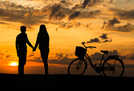 Silhouette of sweet couple in love happy time and bicycle in beautiful sunsetの写真素材