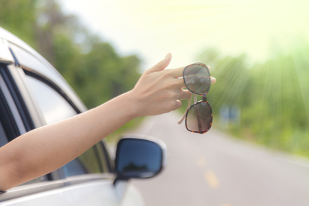 Woman hand at the car window with sunglasses on an country road, Summer vacation conceptの写真素材