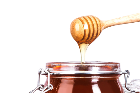 Glass jar of Honey with wooden drizzler on white backgroundの写真素材