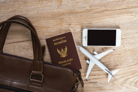Thai passport, Leather bag, Phone and Small plane model on wooden board background, Travel conceptの写真素材