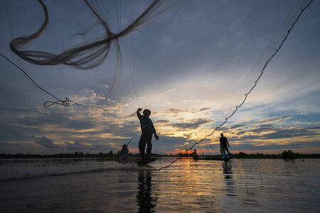 Silhouette of Fisherman on fishing boat with net on the lake at sunset, Thailand