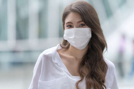 Portrait of young woman wearing medical face mask protective using a phone walks in a cityの写真素材
