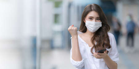 Portrait of young woman wearing medical face mask protective using a phone walks in a cityの写真素材