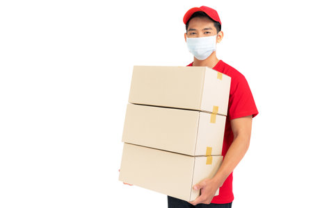 Delivery man employee in red t-shirt uniform face mask holding empty cardboard box isolated on white backgroundの写真素材