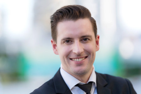 Close up of Smiling businessman standing in front of modern office buildingsの写真素材
