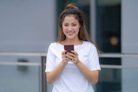 Woman in white t-shirt and blue jeans using laptop sitting on a floor outside in the city street background, Summer dayの写真素材