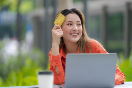 Woman in white t-shirt and blue jeans using laptop sitting on a floor outside in the city street background, Summer dayの写真素材