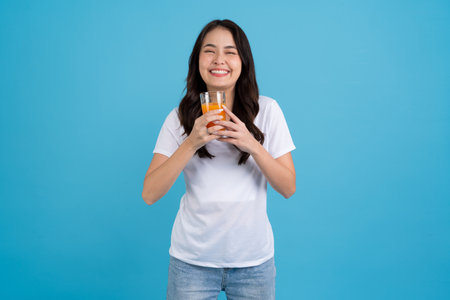Beautiful woman drinking orange from a glass She was wearing a white shirt, smiling, and her eyes were bright. in the blue backgroundの写真素材