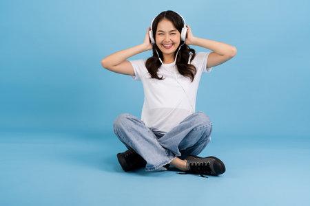 Woman sitting on a blue background Listen to music, enjoy the music, smile brightly, refresh and relax.の写真素材