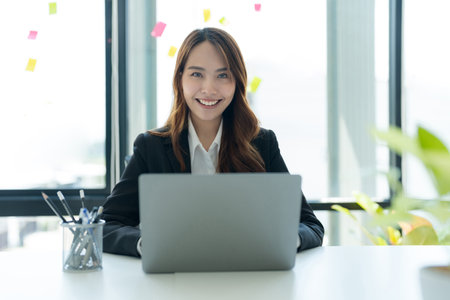 Shot of happy young asian woman looking at camera, Attractive businesswoman working on laptop in her workstation office.の写真素材