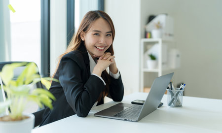 Shot of happy young asian woman looking at camera, Attractive businesswoman working on laptop in her workstation office.の写真素材
