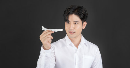 Business man holding a clean white toy plane that means air travel on a dark backgroundの写真素材