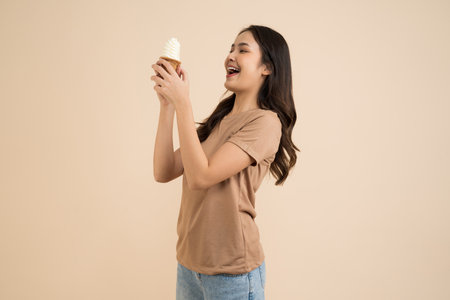 Happy young woman eating ice cream standing on brown backgroundの写真素材