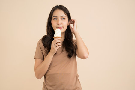 Happy young woman eating ice cream standing on brown backgroundの写真素材