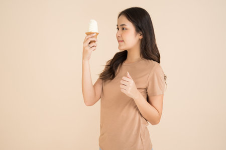 Happy young woman eating ice cream standing on brown backgroundの写真素材