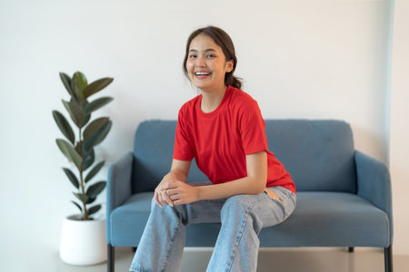 A beautiful woman in a red shirt sitting on the sofa happy smile and feel relaxed.の写真素材