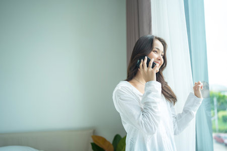 A beautiful woman stood by the window wearing a white shirt and drink plain water to make the body feel refreshed in the morning.の写真素材
