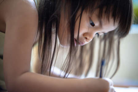 Selective focus is a 3-year-old Asian girl with long black hair sitting on a chair. She was paying attention to the picture book in his hand.の写真素材
