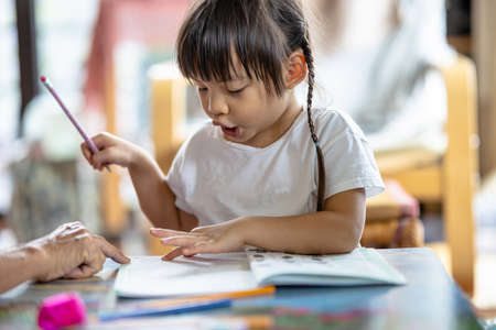 Selective focus of a 3-year-old Asian girl practicing writing and drawing at home with her grandmother due to the COVID-19 pandemic. Concept of learning from home and Practicing small musclesの写真素材