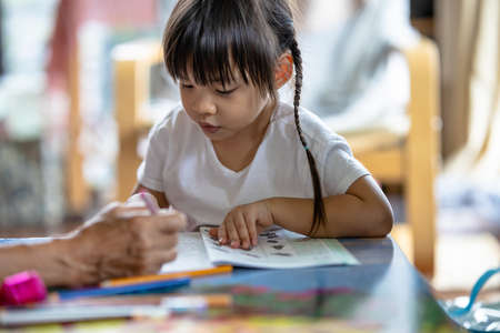 Selective focus of a 3-year-old Asian girl practicing writing and drawing at home with her grandmother due to the COVID-19 pandemic. Concept of learning from home and Practicing small musclesの写真素材