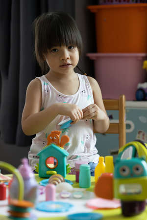 A three-year-old Asian girl with long black hair and a braid. which is the age of innocence and being cute Playing with kitchenware toys, including cups, plates, bowls, fixing spoons and condiment sets. By pretending to be a cook to feed her dolls.の写真素材