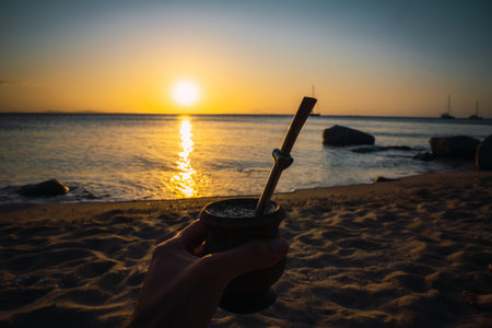 Hand holding yerba mate calabash during beach sunset