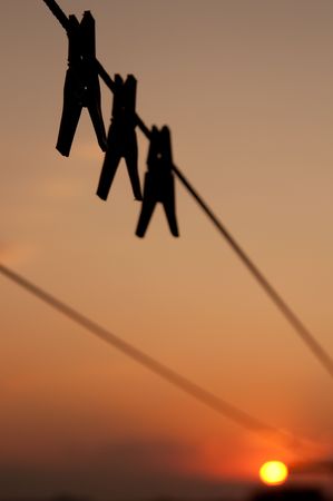Three clothespins weigh on a cord, against an evening declineの写真素材