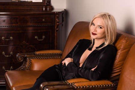 An attractive young girl sits on a beautiful leather sofaの写真素材