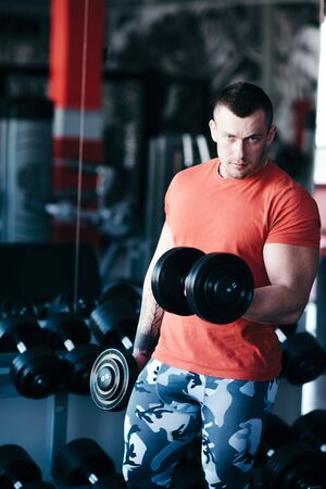 Muscular man training with black dumbbell in the gym. Workout in gymの写真素材
