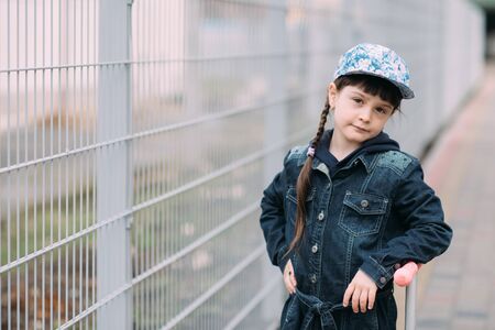 Cute little girl in jeans cardigan and on scooter on the background of the fence. Springの写真素材