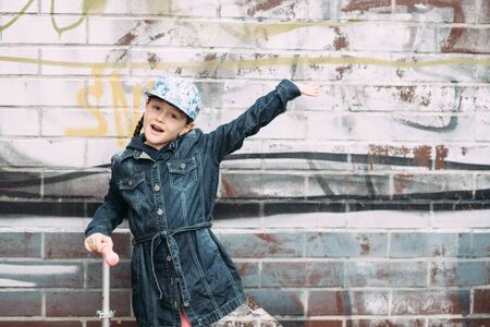 Cute little girl in jeans cardigan and on scooter on the background the urban colorful wall. Springの写真素材