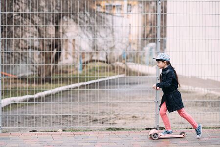 Cute little girl in jeans cardigan riding a scooter on the street. Springの写真素材