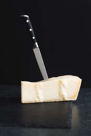 An appetizing solid cheese on a black plate on a gray stone background. Various types of cheeseの写真素材