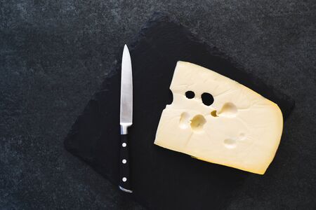 An appetizing solid cheese on a black plate on a gray stone background. Various types of cheeseの写真素材