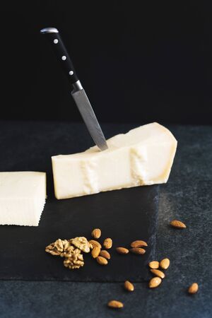 An appetizing solid cheese on a black plate on a gray stone background. Various types of cheeseの写真素材