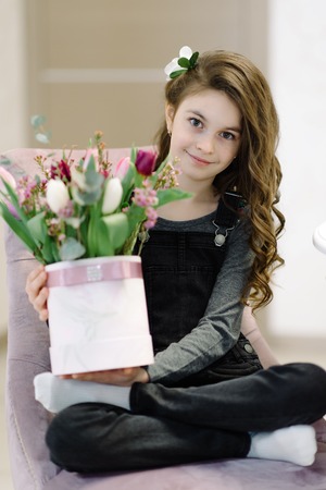 A nice little girl is sitting on the chair with a bouquet of flowers. She enjoys spring and sun. The concept of happy people, children.の写真素材