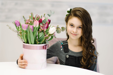 A nice little girl is sitting on the chair with a bouquet of flowers. She enjoys spring and sun. The concept of happy people, children.の写真素材
