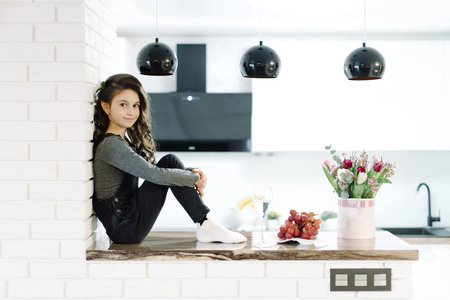 A cute little girl sits in the kitchenの写真素材