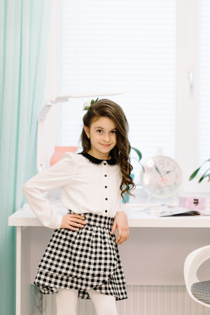 A pretty girl in her room is standing next to the table. Beautiful interior room for the children's roomの写真素材