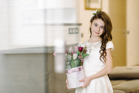 A cute girl sits on a sofa and holds flowers in her hands. Feast dayの写真素材